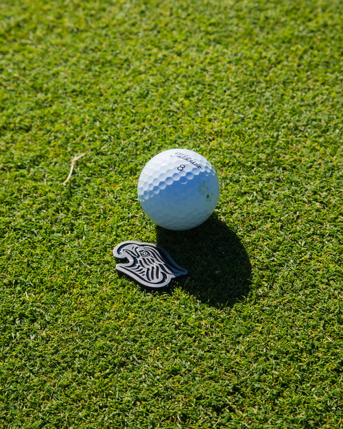 Golf ball on a green grass marked with eagle shaped metal ball marker 